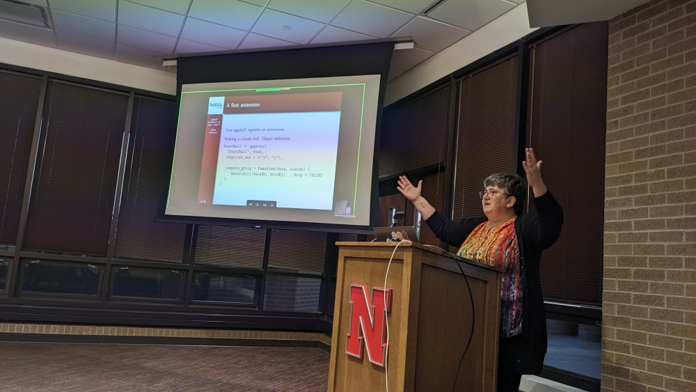 Dr. Heike Hofmann standing in front of a wooden podium gesturing with slide titled 'A first extension' in the background.